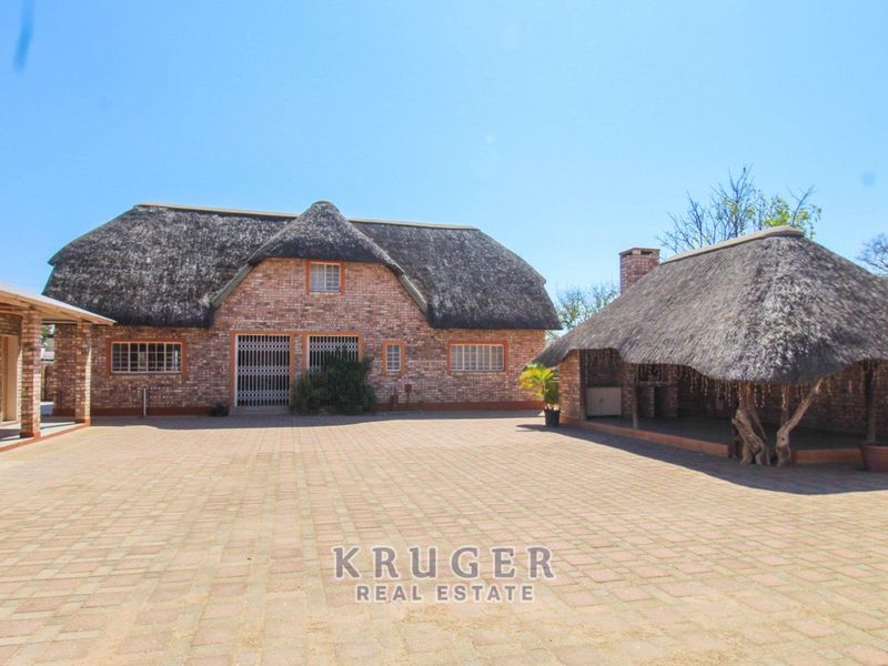 Spacious paved rear courtyard featuring a traditional thatched-roof main building and a separate covered outdoor entertainment area with a built-in braai.