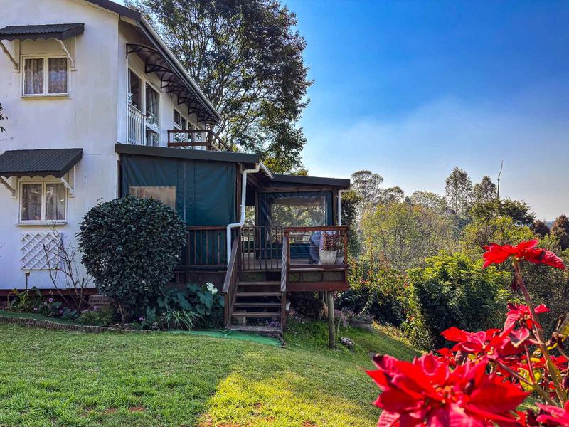 Rear view of the property featuring a raised timber deck with a covered patio area, overlooking the garden and surrounding landscape.