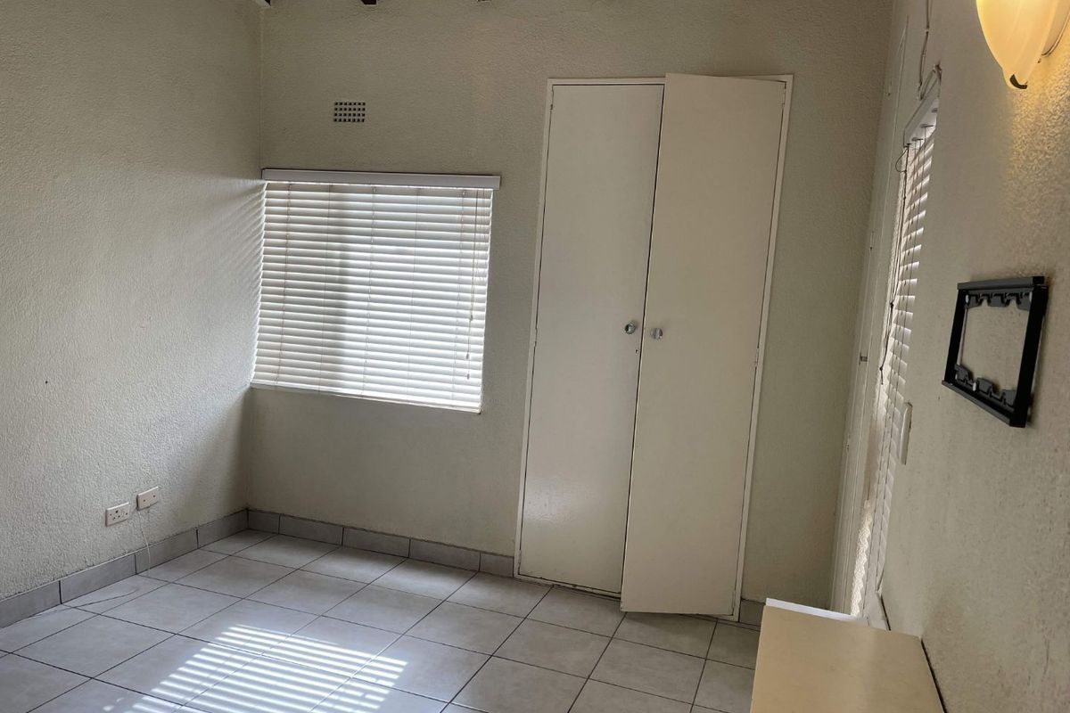 A bedroom featuring tiled flooring, built-in cupboards, exposed ceiling beams, and venetian blinds.