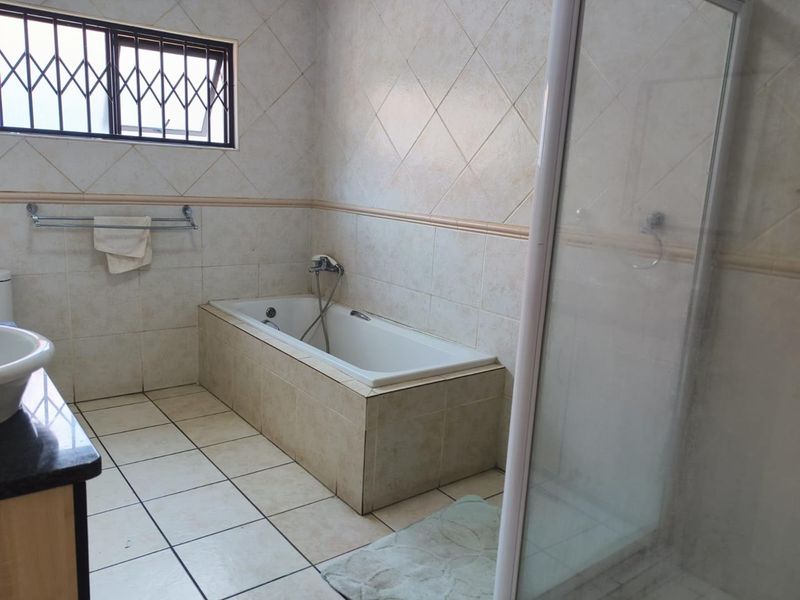 A functional bathroom featuring a built-in bathtub, separate shower enclosure, and vanity basin with tiled finishes throughout.