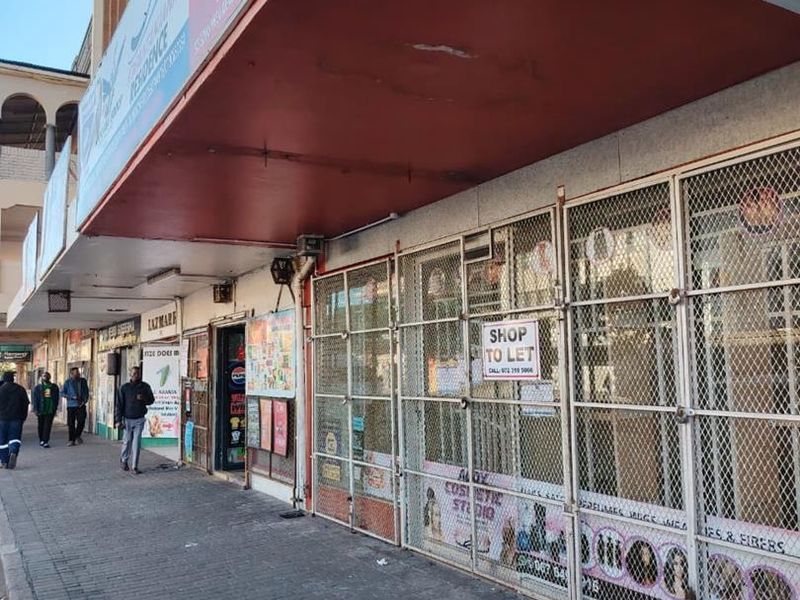 Street-level view of a commercial shopfront featuring metal security gates, signage, and a covered walkway in a busy urban retail area.