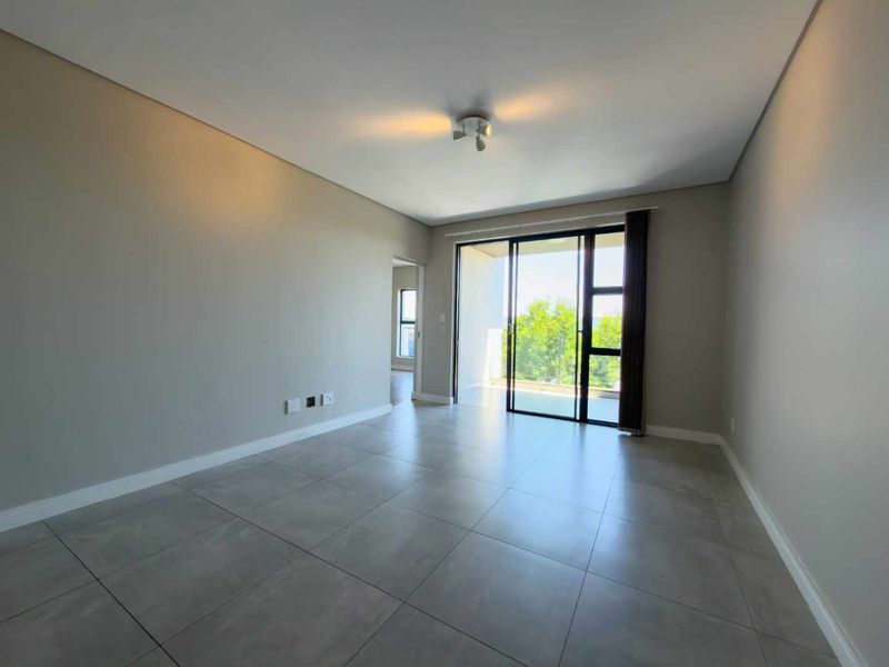 A bright, empty living room featuring neutral tiled flooring and a large sliding glass door providing access to an outdoor balcony area.