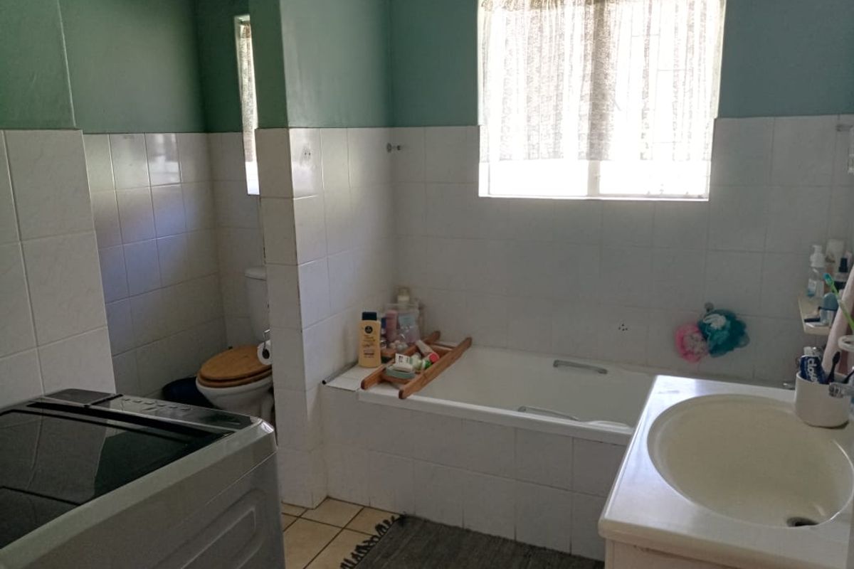 A functional bathroom featuring a built-in bathtub, vanity basin, and toilet with tiled finishes, requiring cosmetic updates to modernize the space.