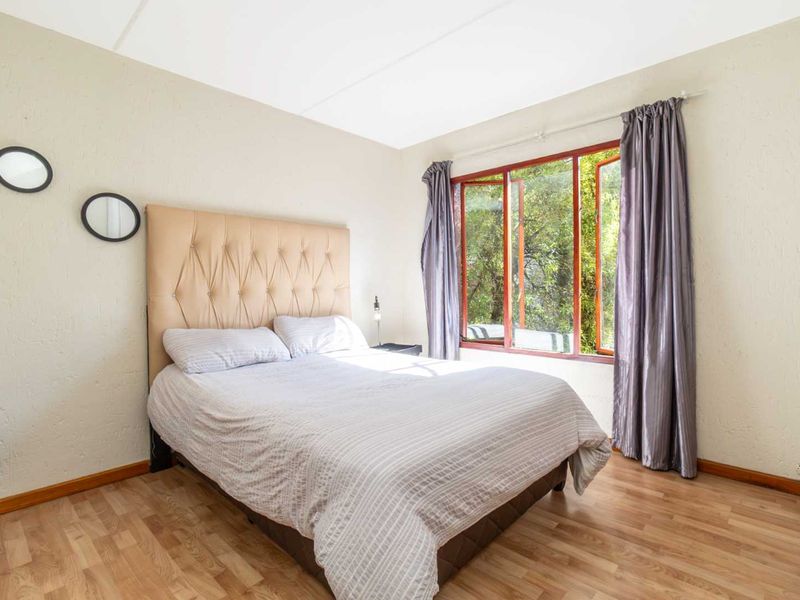 A bedroom featuring laminate flooring and timber-framed windows with natural light.