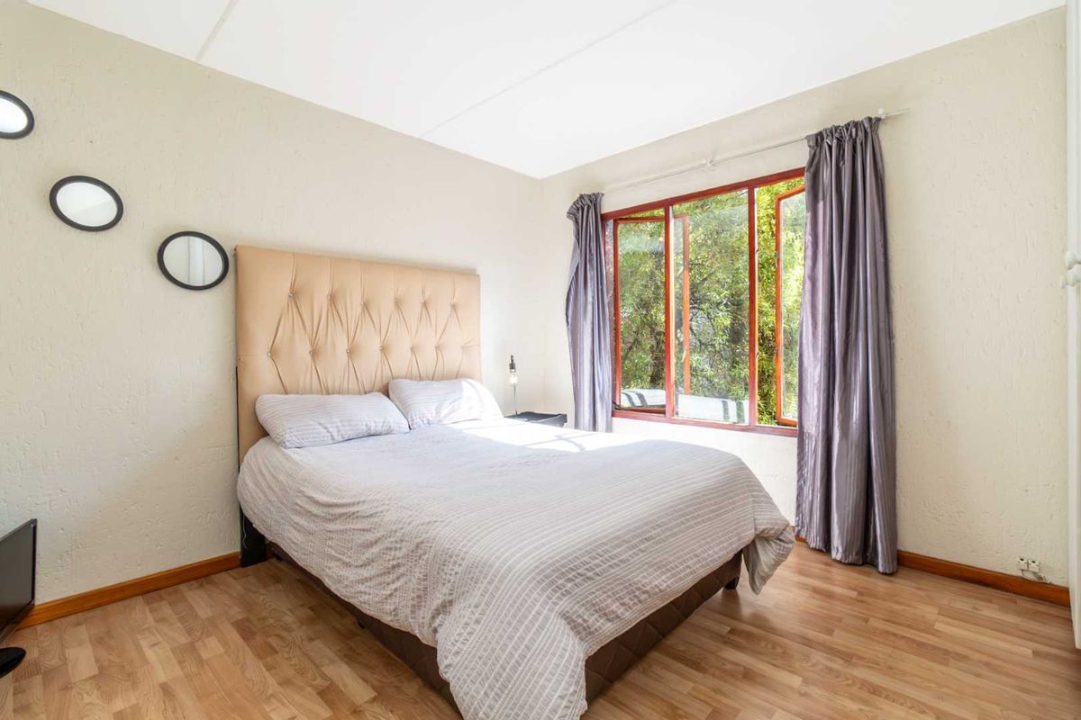 A bedroom featuring laminate flooring and timber-framed windows with natural light.