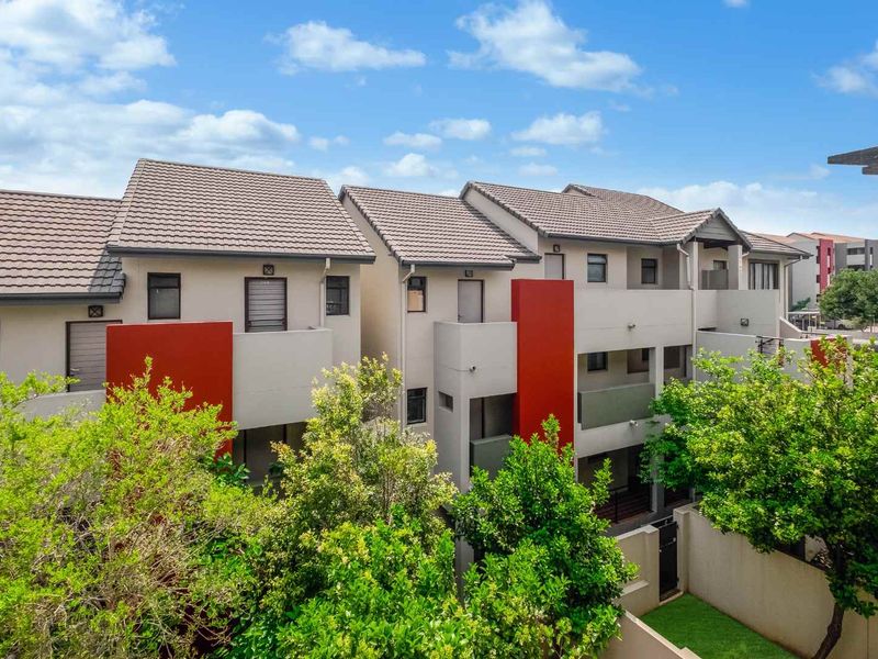 A view of the rear elevation of a modern apartment complex featuring tiled roofs, balconies, and landscaped garden areas.