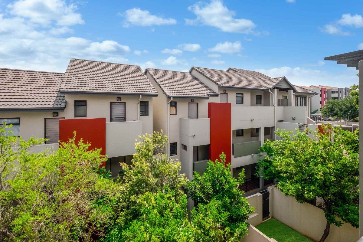 A view of the rear elevation of a modern apartment complex featuring tiled roofs, balconies, and landscaped garden areas.