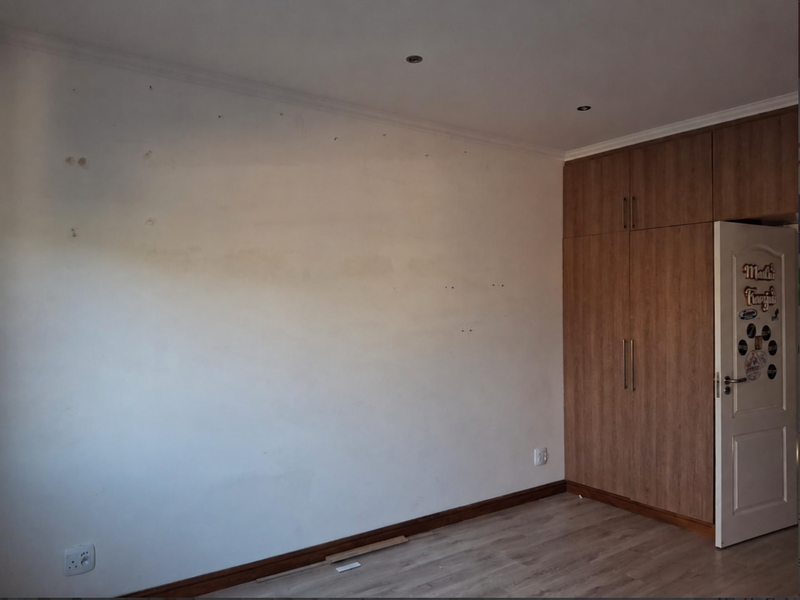 A bedroom featuring built-in wooden cupboards, laminate flooring, and recessed lighting, currently vacant and requiring minor wall repairs and finishing touches.