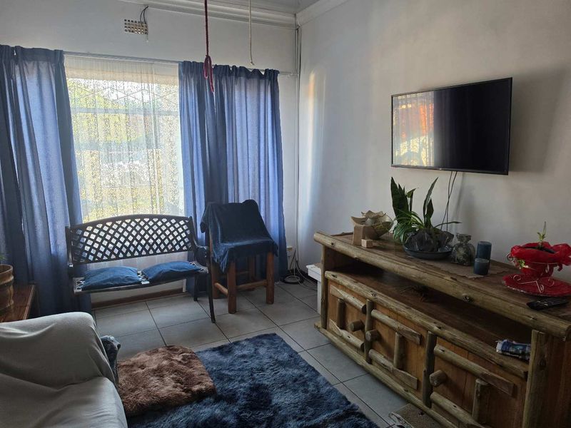 A living room featuring tiled flooring, ceiling cornice, and a wall-mounted television, offering a functional space for relaxation.