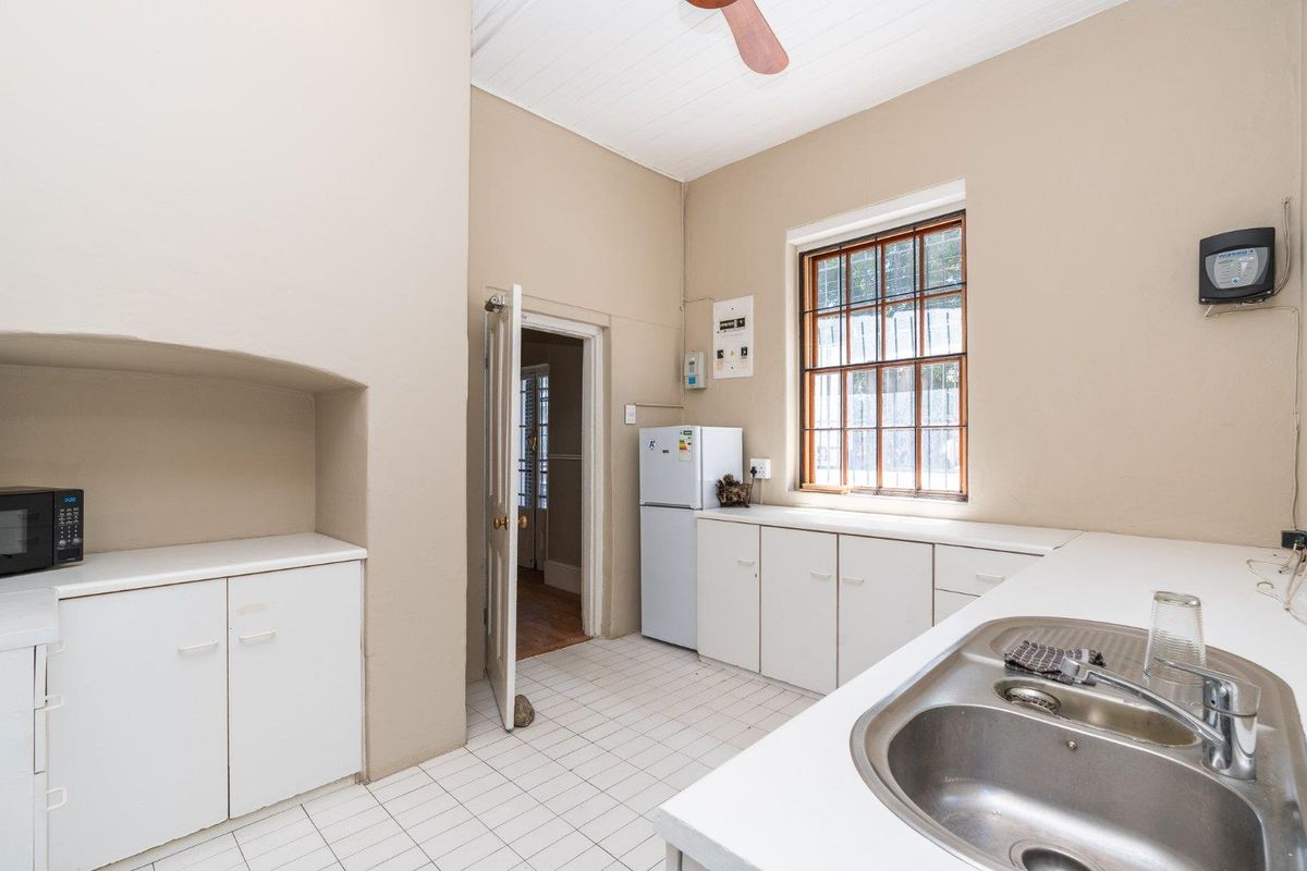A functional kitchen featuring built-in cabinetry, a stainless steel sink, tiled flooring, and a timber-framed window, offering a practical layout for daily use.