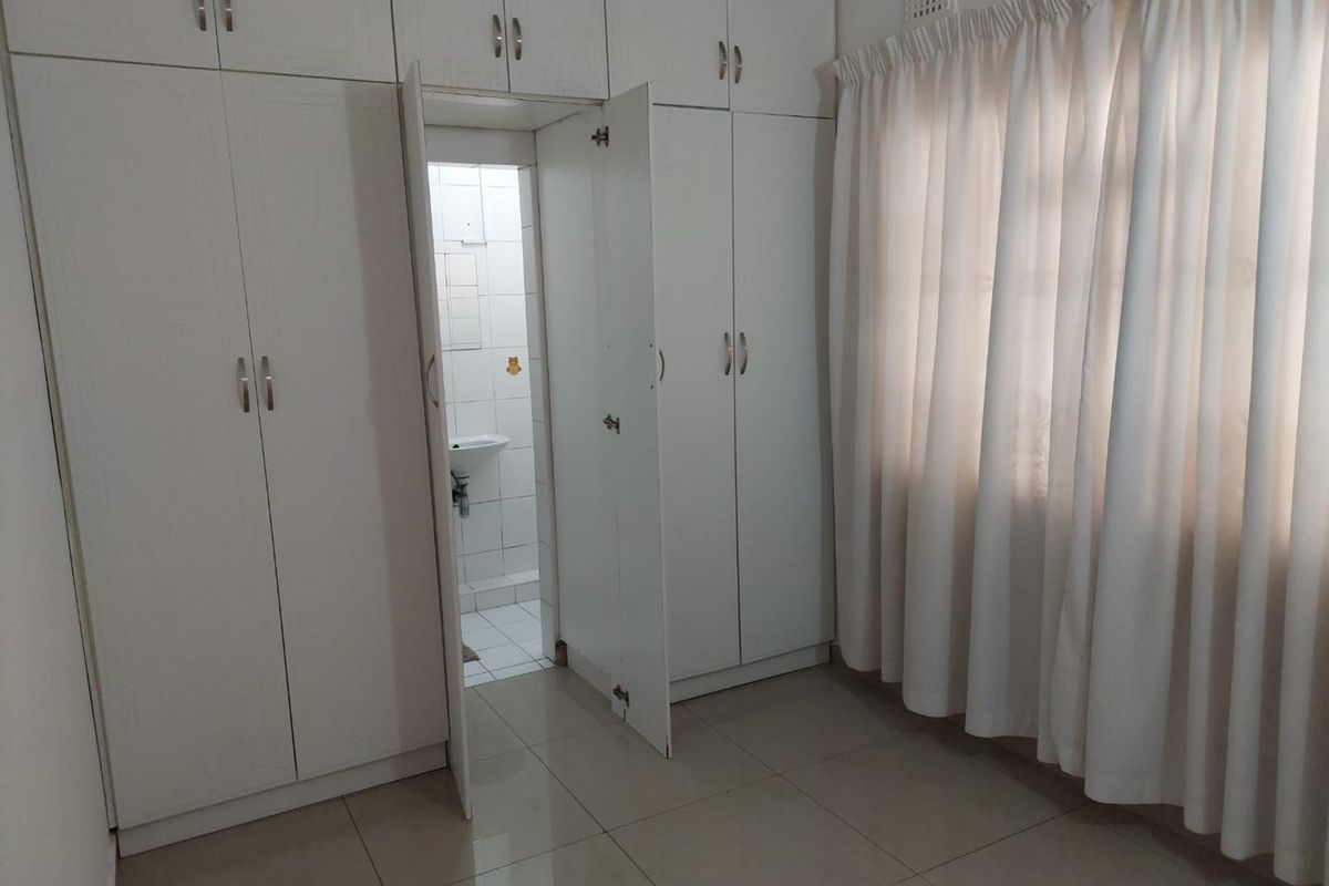 A clean, empty bedroom featuring built-in cupboards, tiled flooring, and an en-suite bathroom access.