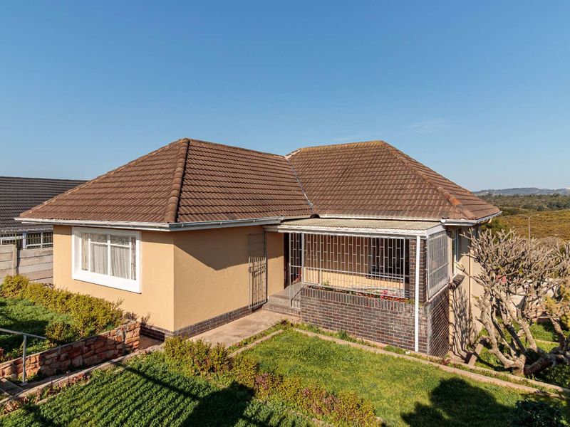 Front view of a single-story house featuring a tiled roof, brick accents, and a secure entrance area with a concrete pathway and landscaped garden.