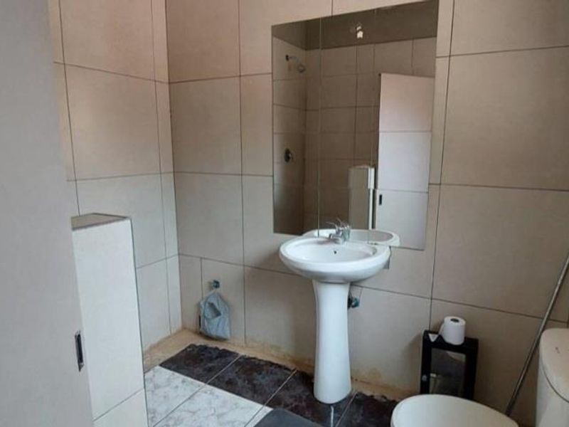 A functional bathroom featuring full-height ceramic wall tiling, a pedestal basin with a wall-mounted mirror, and a standard toilet.