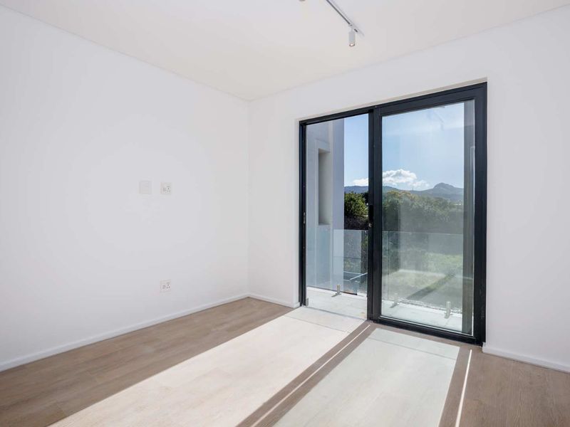 A bright, empty bedroom featuring modern laminate flooring, track lighting, and a large sliding glass door providing access to an outdoor balcony.