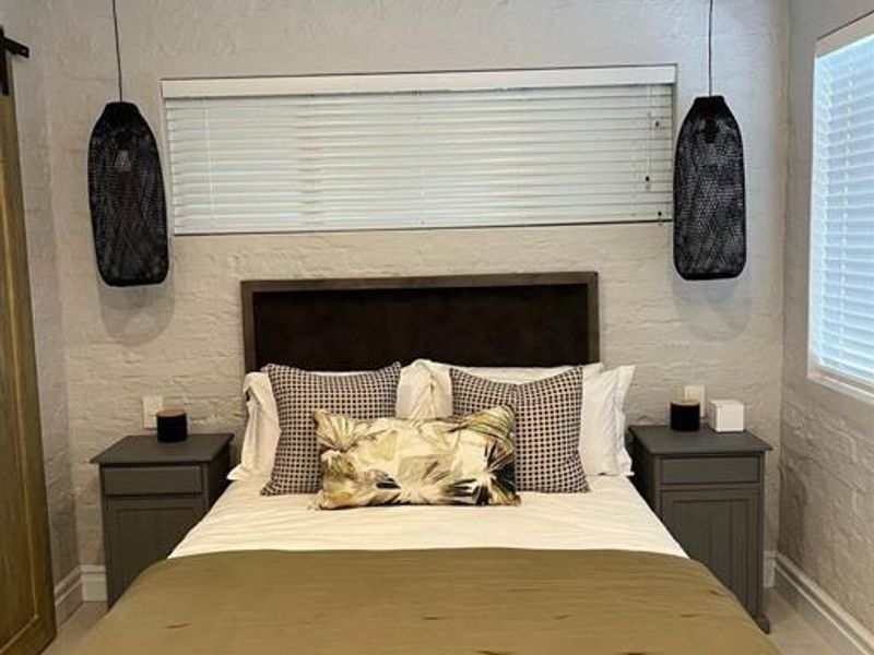 A cozy bedroom featuring exposed white timber rafters, painted brick walls, and a sliding barn door, creating a charming cottage aesthetic.