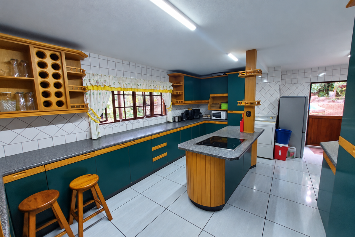 Spacious kitchen featuring dark green and wood-tone cabinetry, a central island with an electric hob, tiled flooring, and ample counter space.