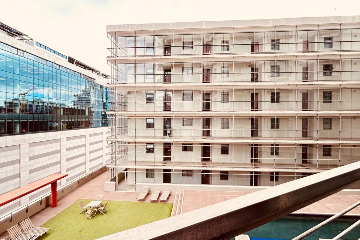 View of a modern apartment complex exterior featuring a swimming pool, wooden decking, and multi-level balconies with glass railings.