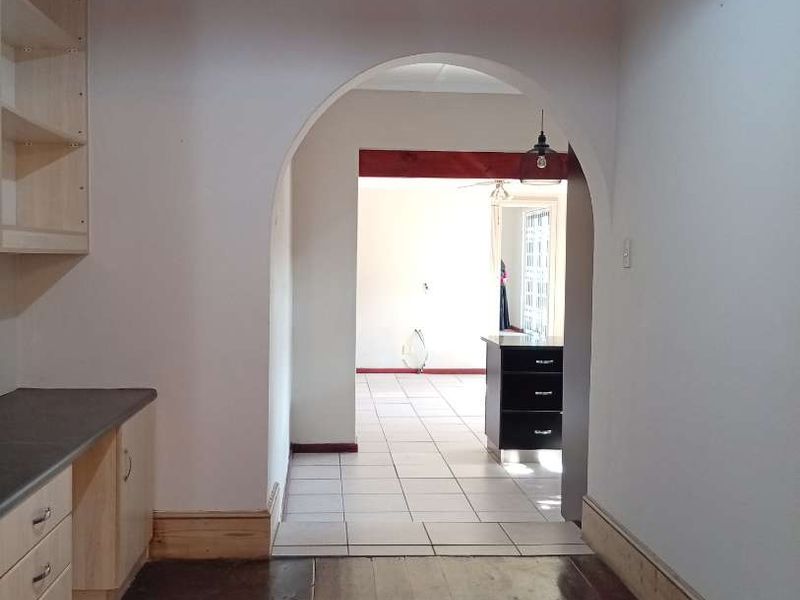 A functional kitchen area featuring built-in cabinetry and timber flooring, leading through an archway into an adjacent tiled living space.