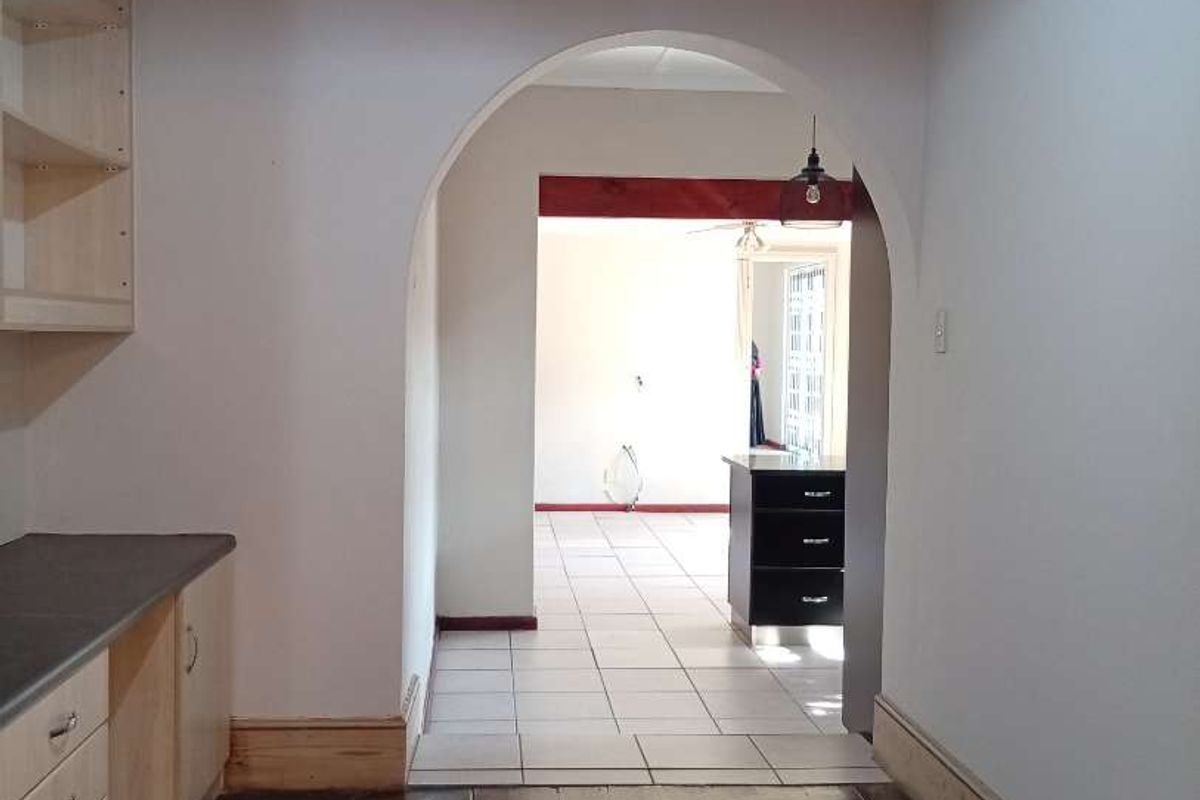 A functional kitchen area featuring built-in cabinetry and timber flooring, leading through an archway into an adjacent tiled living space.