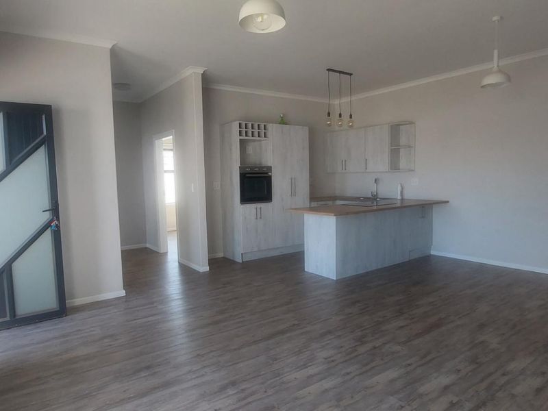 Spacious open-plan living area featuring modern laminate flooring, a functional kitchen with built-in oven, and a central island, offering a bright and versatile layout.