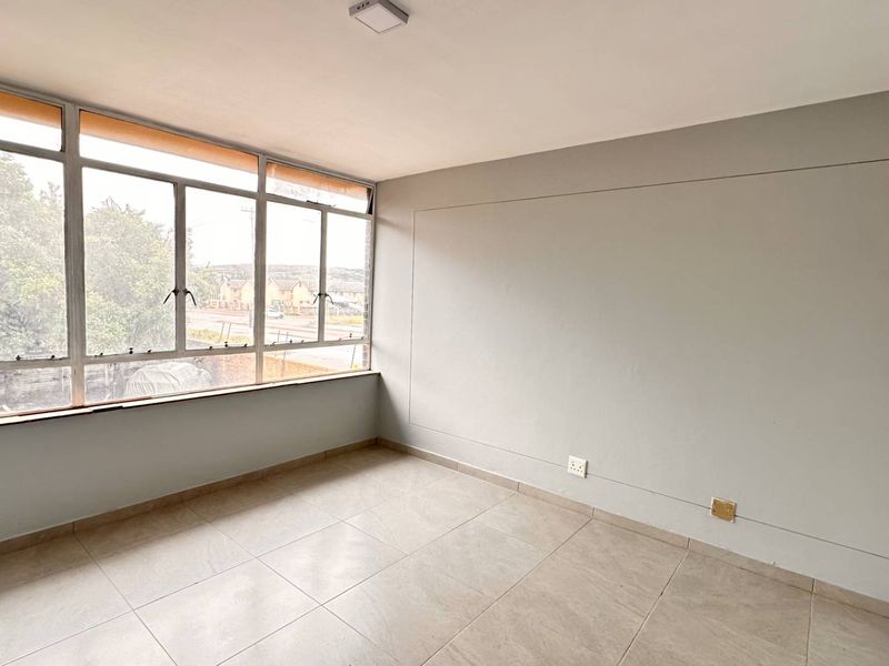 A bright, empty bedroom featuring neutral tiled flooring, built-in cupboards, and large windows providing ample natural light.