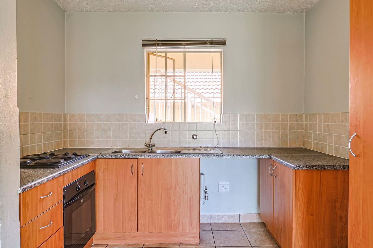 A functional kitchen featuring light wood cabinetry, granite-look countertops, a built-in oven and hob, and a tiled splashback with a window view.