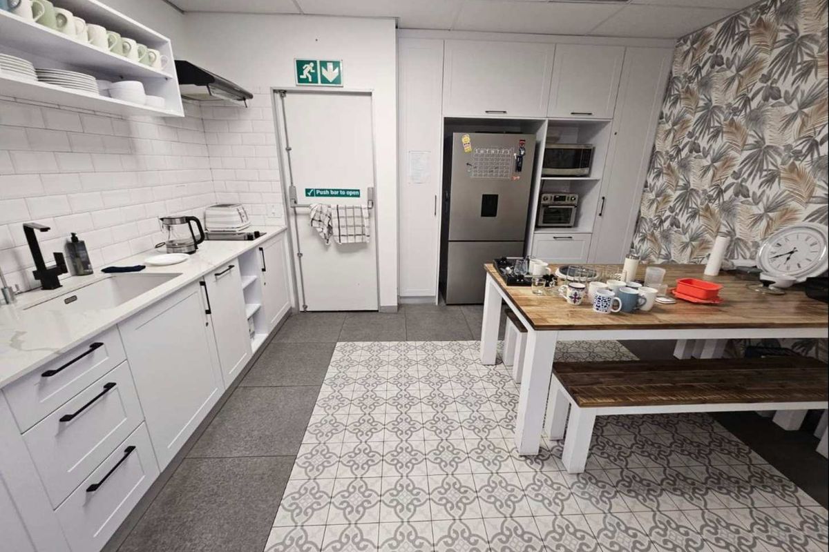 A modern office kitchen featuring white cabinetry, integrated appliances, tiled flooring, and a dedicated dining area with patterned floor accents.