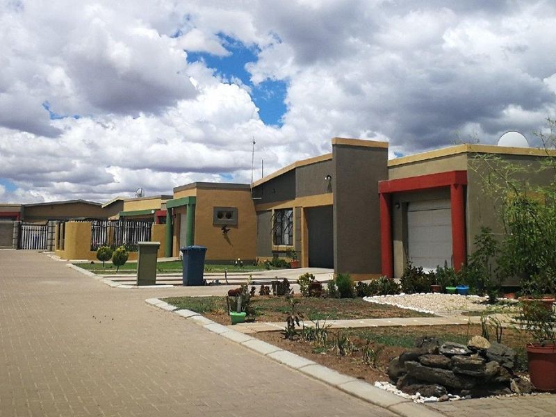 A view of the front exterior of a residential property featuring a paved driveway, garage access, and boundary walling within a complex setting.