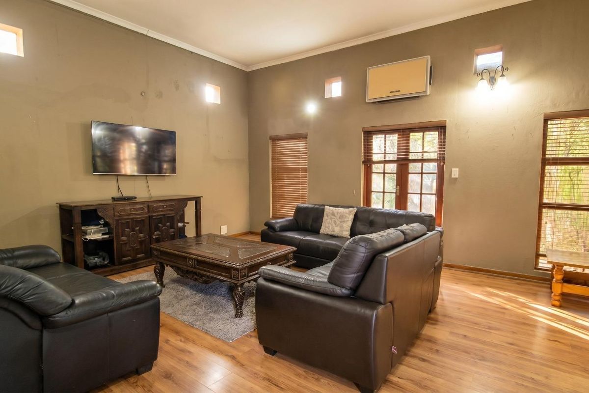 Spacious living room featuring wood-look laminate flooring, high ceilings, wall-mounted air conditioning unit, and multiple windows with wooden blinds.