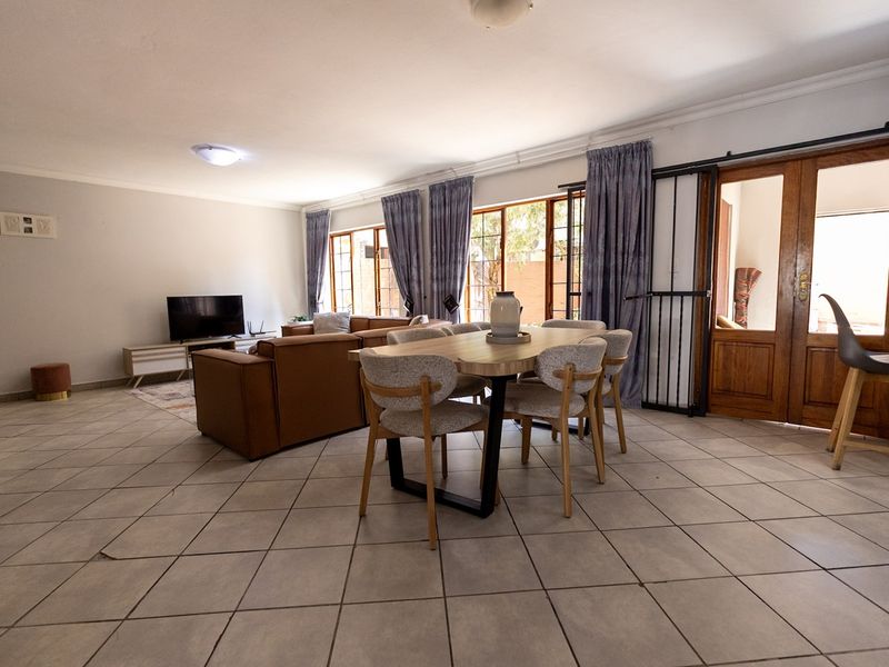 Spacious open-plan living and dining area featuring tiled flooring and direct access to the exterior through wooden framed glass doors.