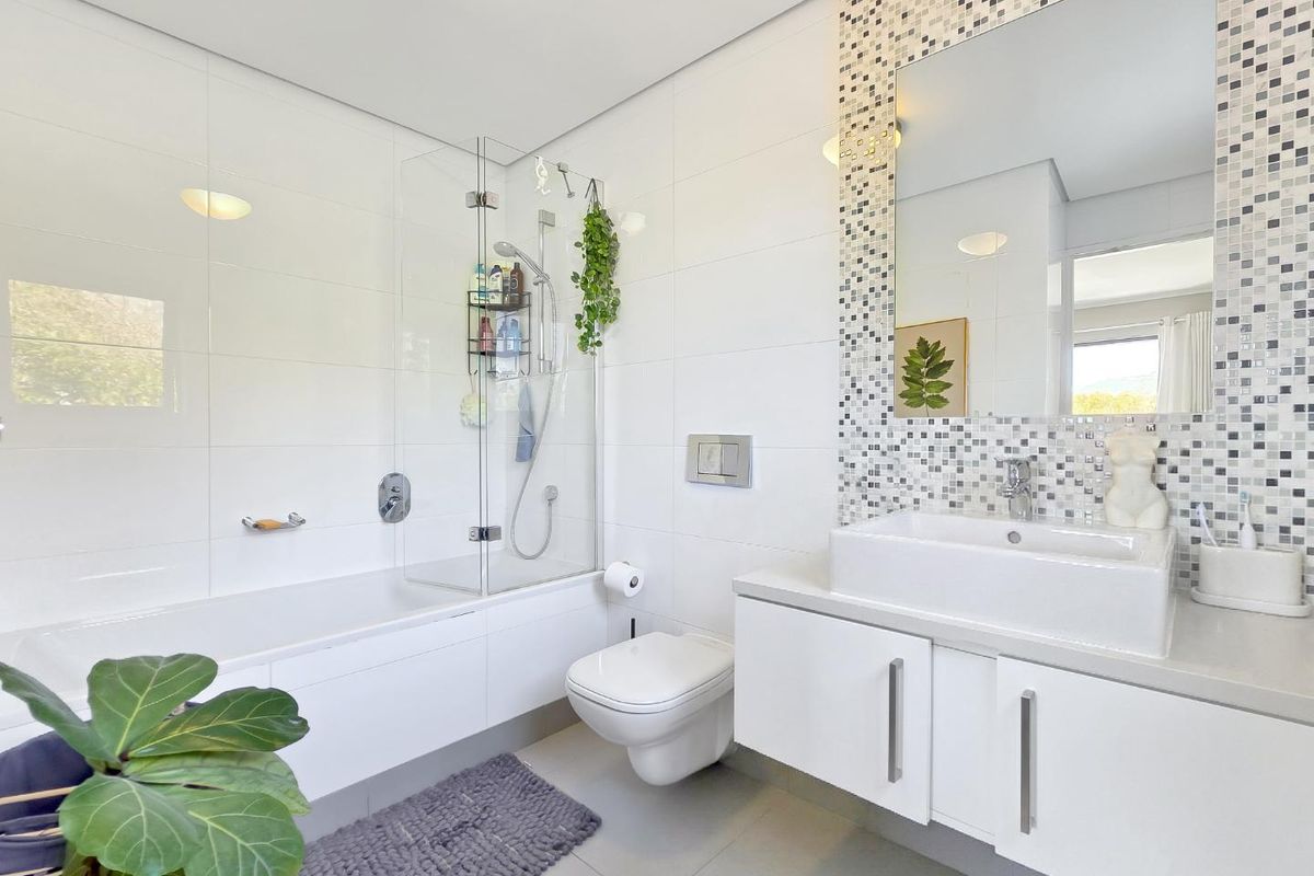Modern bathroom featuring a floating vanity with vessel sink, wall-mounted toilet, and a built-in bathtub with a glass shower screen and mosaic tile accents.