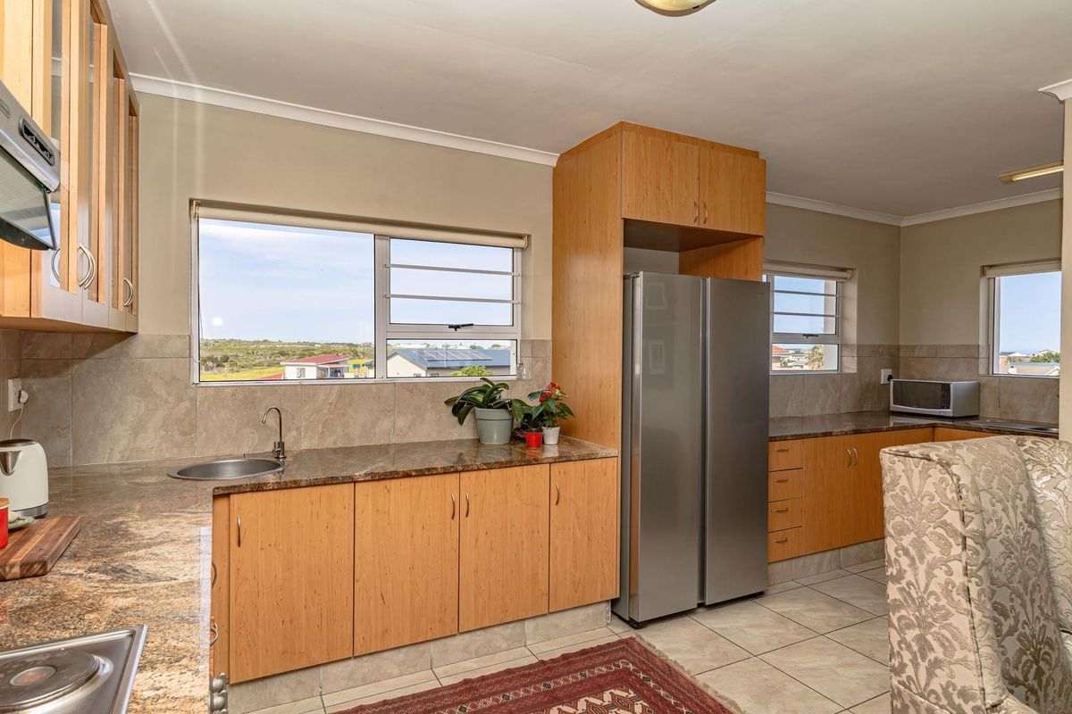 A functional kitchen featuring granite countertops, wooden cabinetry, tiled backsplash, and louver windows with views of the surrounding area.