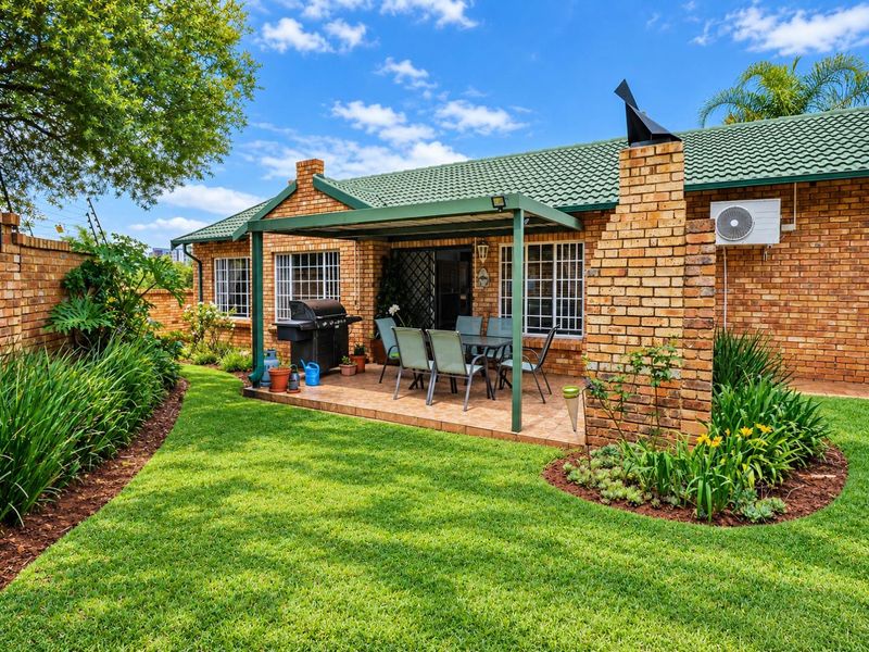 A well-maintained rear garden featuring a paved patio area with a metal pergola, brick chimney, and established landscaping.