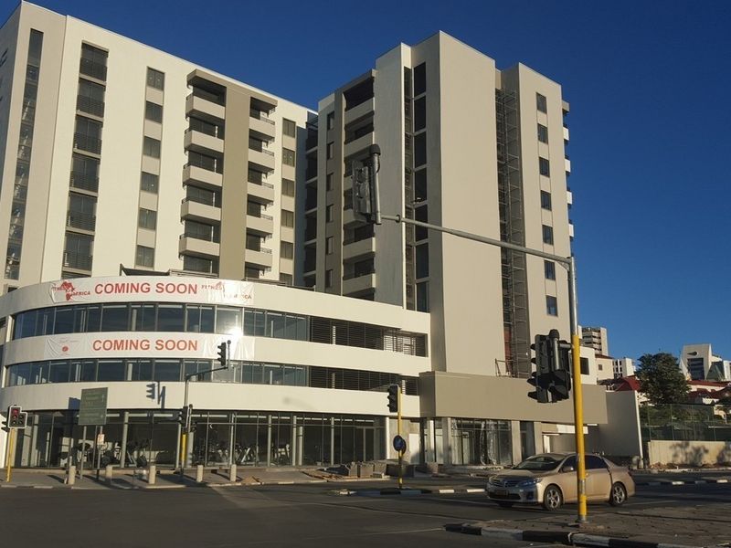 A modern multi-story apartment building featuring a prominent glass-fronted commercial level at street view, showcasing contemporary architectural design and urban positioning.