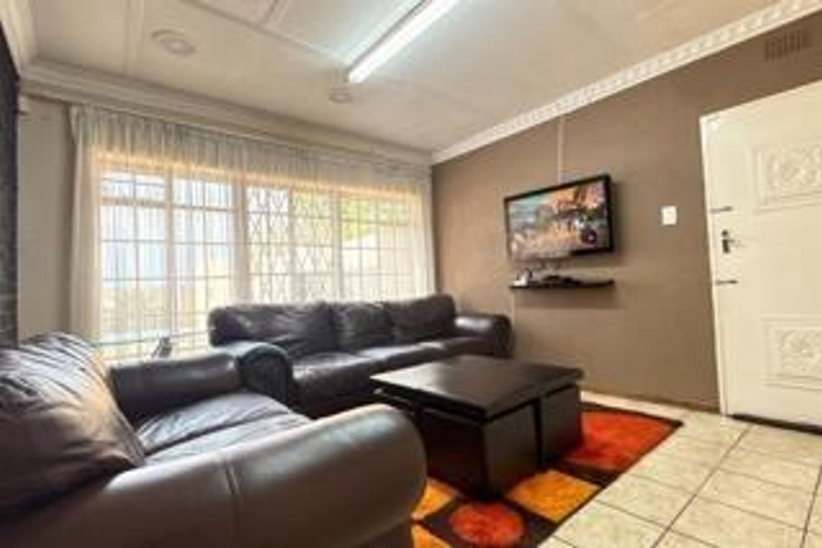 A living room featuring tiled flooring, decorative ceiling cornices, and large windows with security bars.