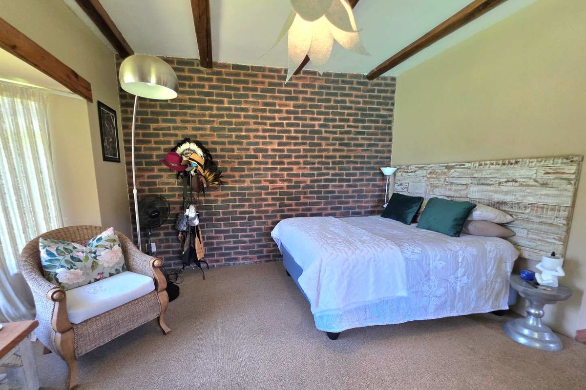 A bedroom featuring a prominent exposed brick feature wall, exposed timber ceiling beams, and neutral carpeting.