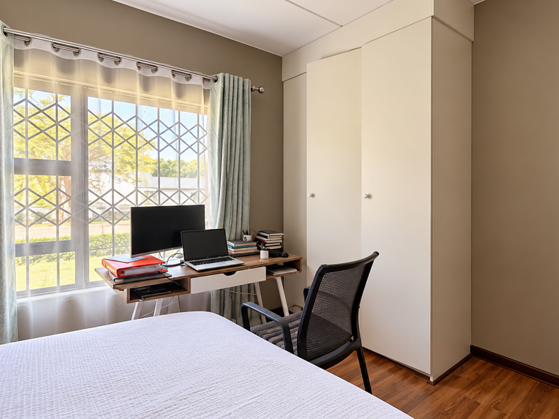 A well-maintained bedroom featuring laminate flooring, a built-in wardrobe, and a window with security bars, providing a functional and bright living space.