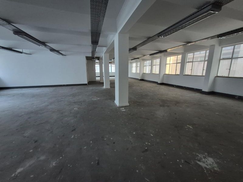 A spacious, open-plan office area featuring exposed ceiling lighting, structural columns, and large windows providing ample natural light, ready for custom fit-out.