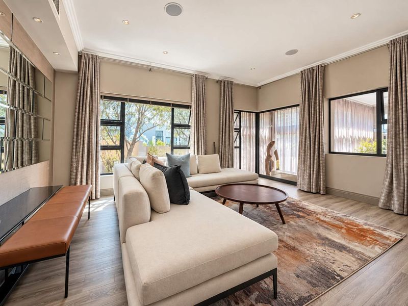 A bright and modern living room featuring large aluminium-framed windows, recessed ceiling lighting, integrated speakers, and elegant mirrored wall accents.