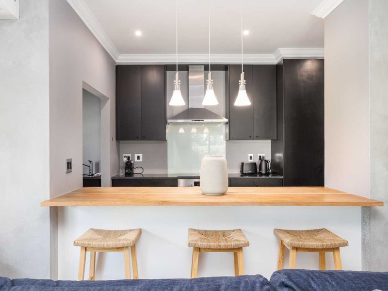 Modern kitchen featuring dark cabinetry, integrated appliances, a wooden breakfast bar, and stylish pendant lighting, creating a functional and contemporary cooking space.