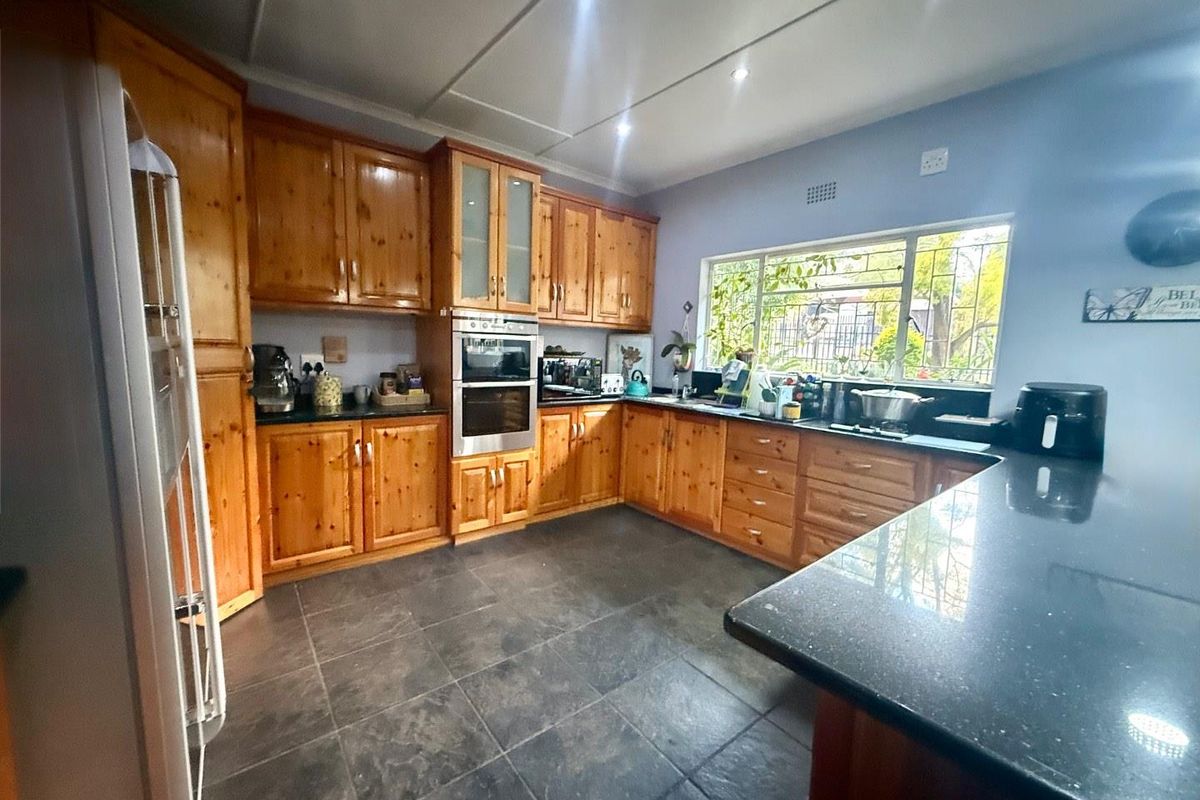A functional kitchen featuring wooden cabinetry, dark stone countertops, built-in oven, and tiled flooring with ample natural light from the window.