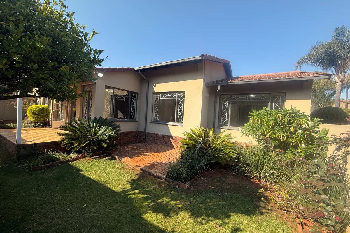 Rear view of the townhouse featuring a brick-paved patio, landscaped garden, and terracotta tiled roof with security-fitted windows.