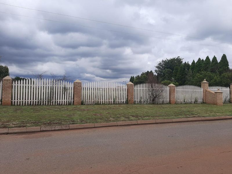 A view of the property boundary featuring a white picket fence supported by brick pillars along the street frontage.