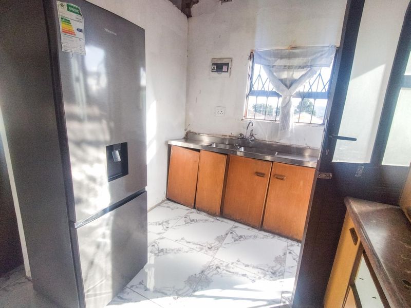 A compact kitchen area featuring built-in wooden cabinetry, a stainless steel sink, and tiled flooring, requiring cosmetic updates to the walls and finishes.