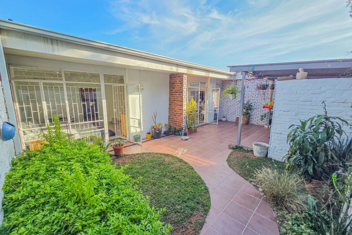 Rear exterior view featuring a tiled patio area, covered pergola, and direct access to the interior through glass sliding doors with security gates.