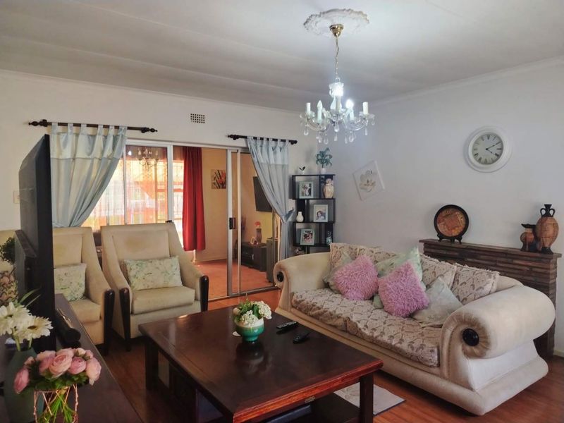 A comfortable living room featuring a classic chandelier, ceiling rose, and sliding glass doors leading to an adjacent space, with warm laminate flooring throughout.