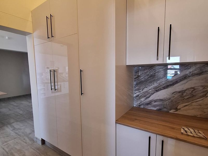 Modern kitchen featuring high-gloss cabinetry, a marble-look splashback, and a wood-look countertop, offering a clean and contemporary aesthetic.
