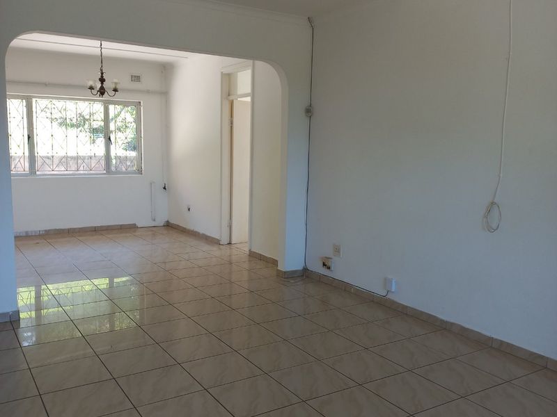 An empty, open-plan living area featuring tiled flooring, an arched transition, and large windows with security bars, offering a blank canvas for interior design.