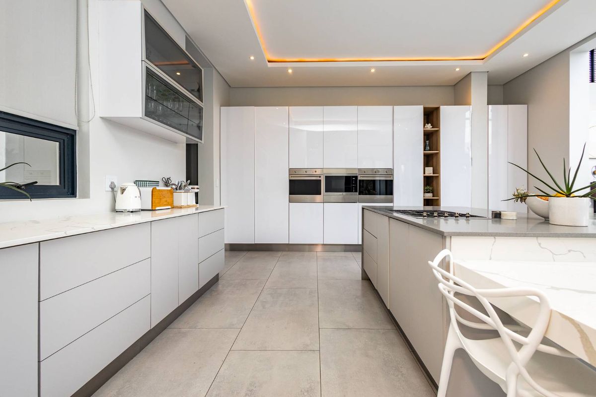 Modern kitchen featuring high-gloss white cabinetry, integrated ovens, a central island with a cooktop, and recessed ceiling lighting.