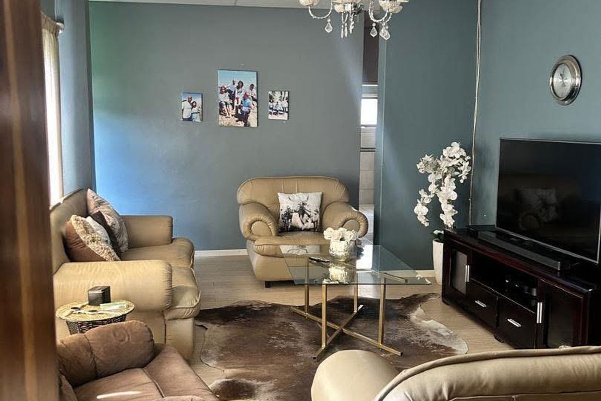 A living room featuring blue painted walls, light wood-look flooring, and a suspended ceiling with a central chandelier.